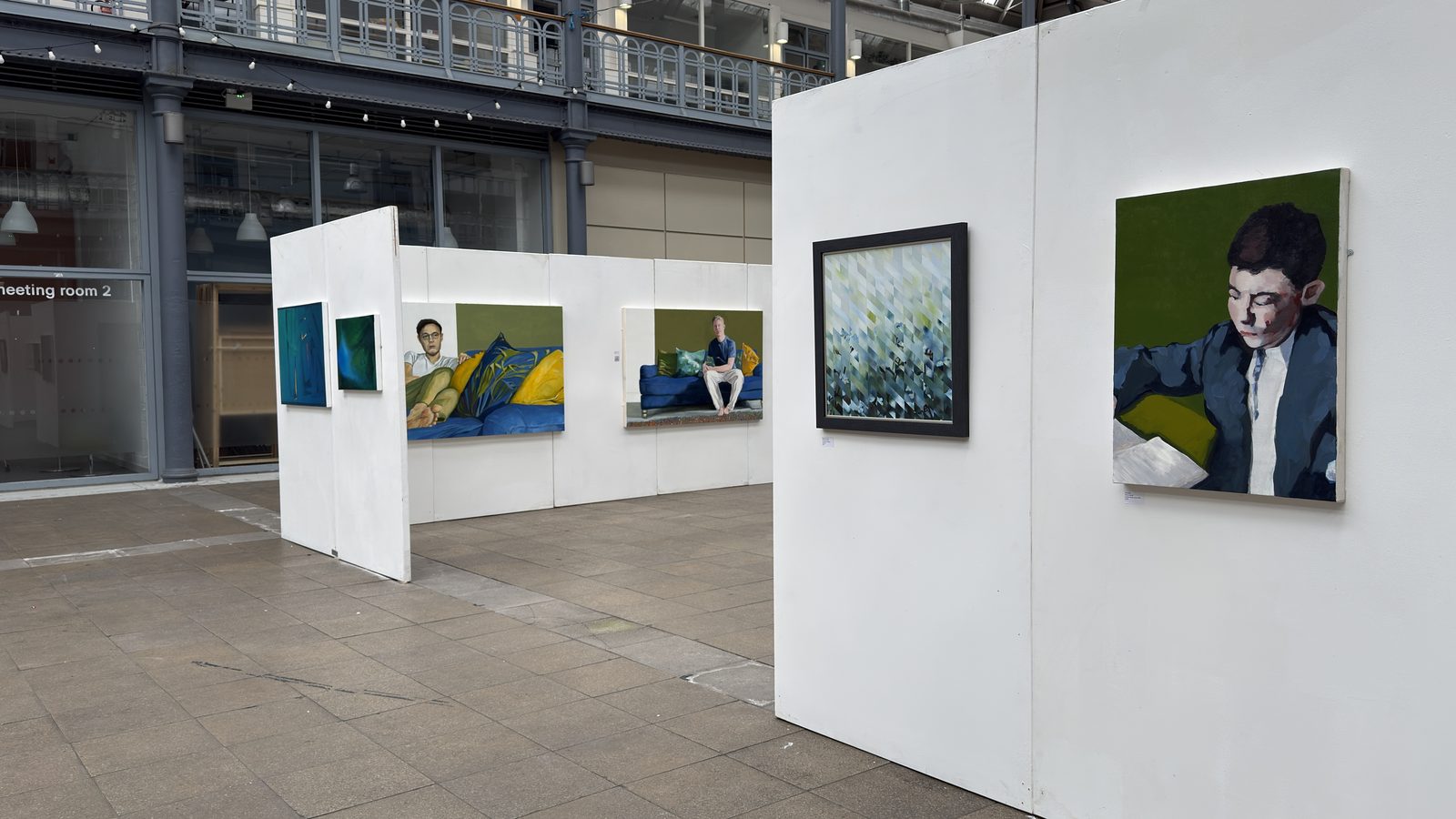 Installation view: two large sofa paintings on a freestanding white wall, with Chrysalis, a boy reading, on the nearest panel.