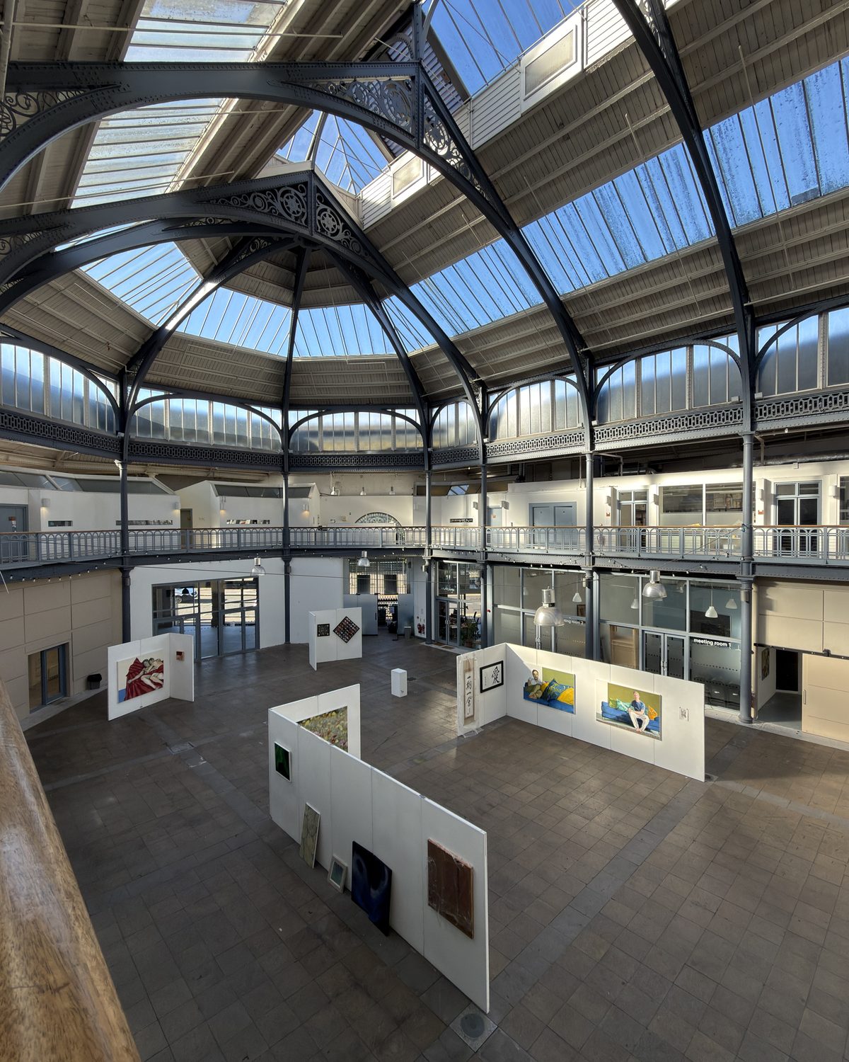 Looking down into The Briggait's atrium from the gallery level, with the exhibition panels on the floor beneath the cast-iron and glass roof.